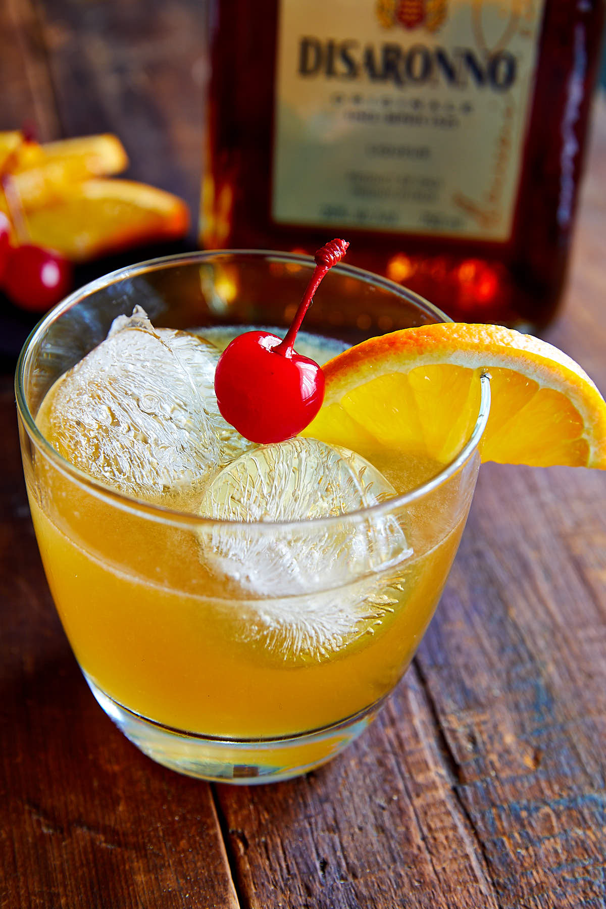 Close up of amaretto sour drink in a glass with ice, orange slice and a maraschino cherry.