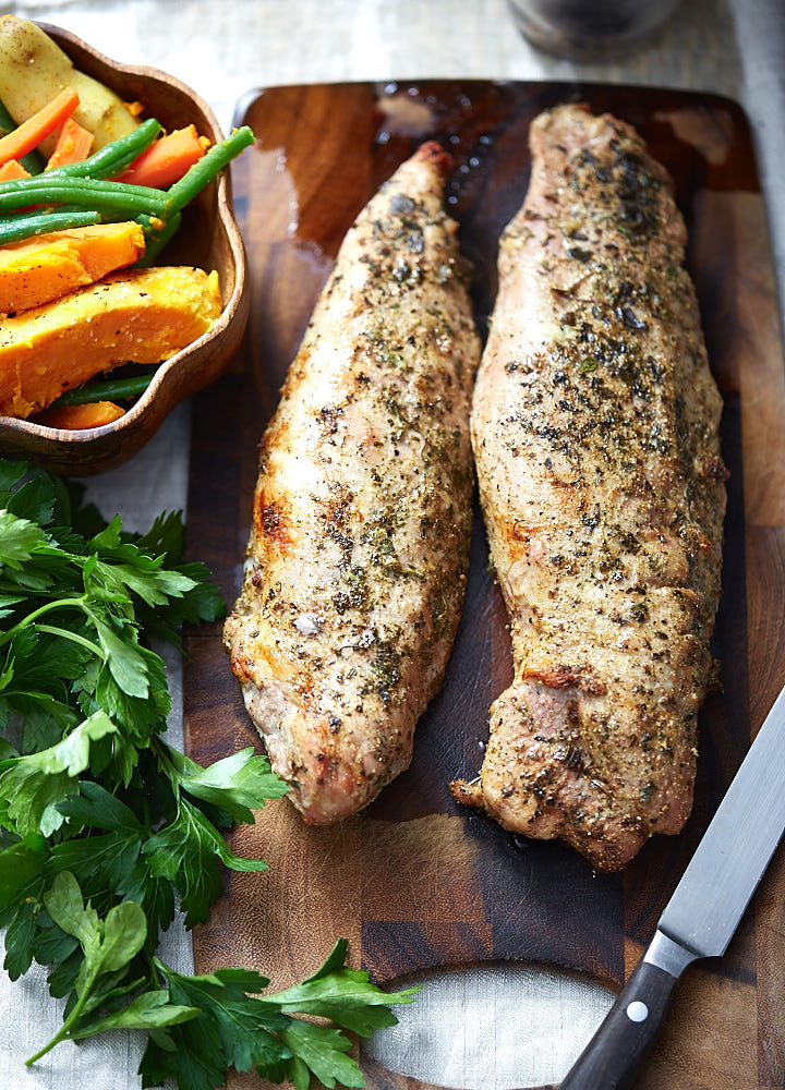 Two pork tenderloins on a cutting board with vegetables next to them.