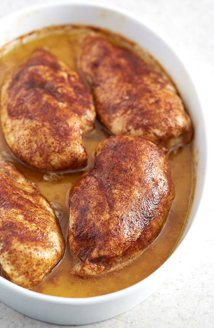 Succulent chicken breasts inside a white baking dish with pan juices.