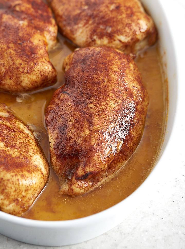 Close up of a large slow baked chicken breast, moist and juicy, inside a baking dish with pan juices.