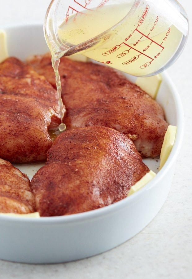 Pouring chicken broth into a baking dish with chicken breasts.