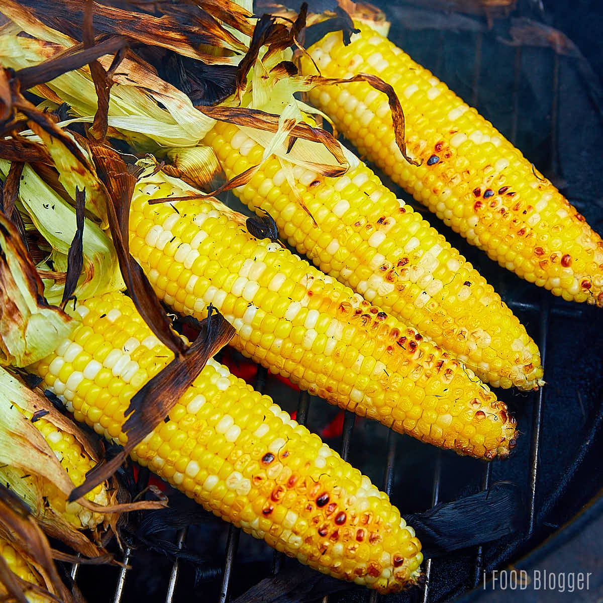 Corn without husks on a charcoal grill.