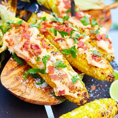 Close up of grilled corn on the cob slathered with mayo and topped with bacon and Parmesan cheese.