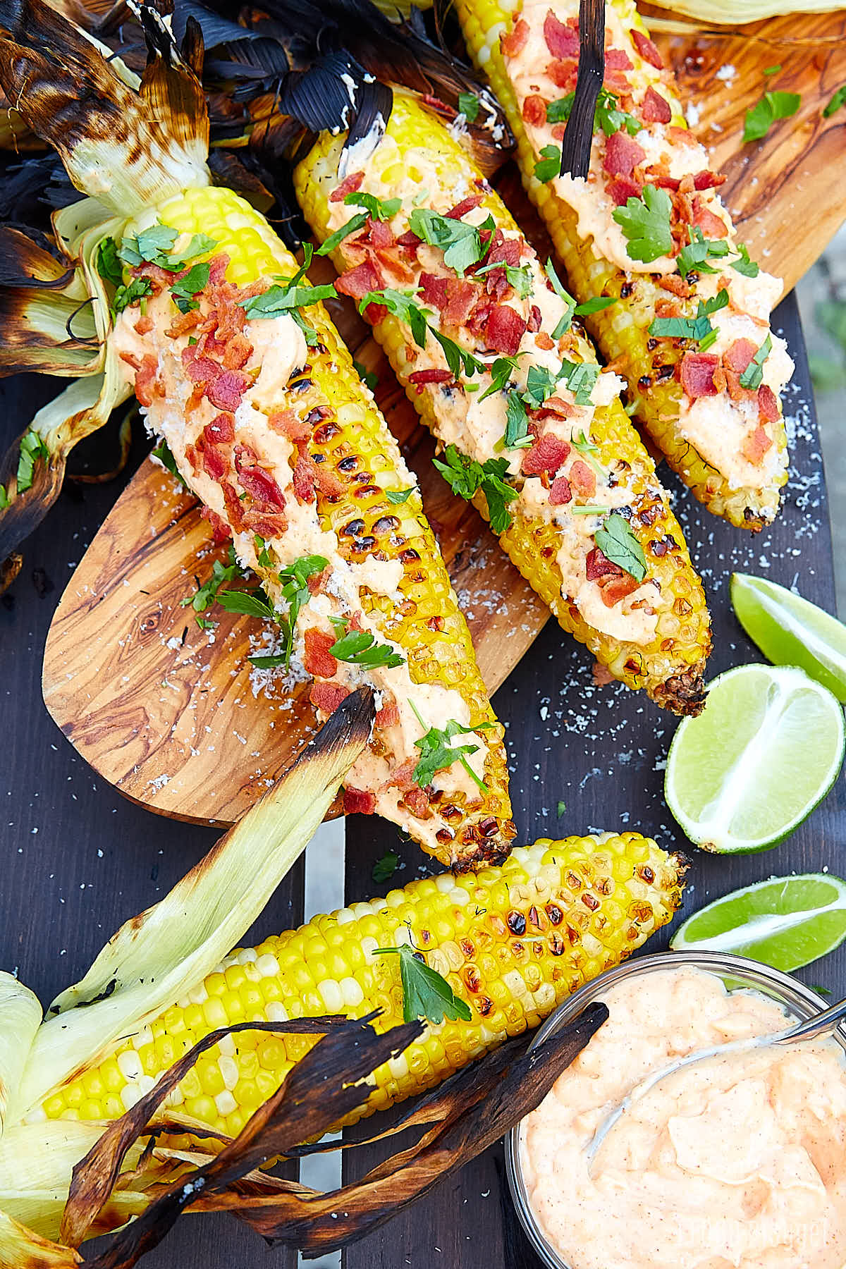 Top down view of corn on the cob, grilled and garnished with garlic mayo, bacon bits and chopped parsley.