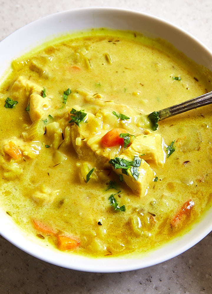 Close up of a spoonful of mulligatawny soup inside a bowl of soup.