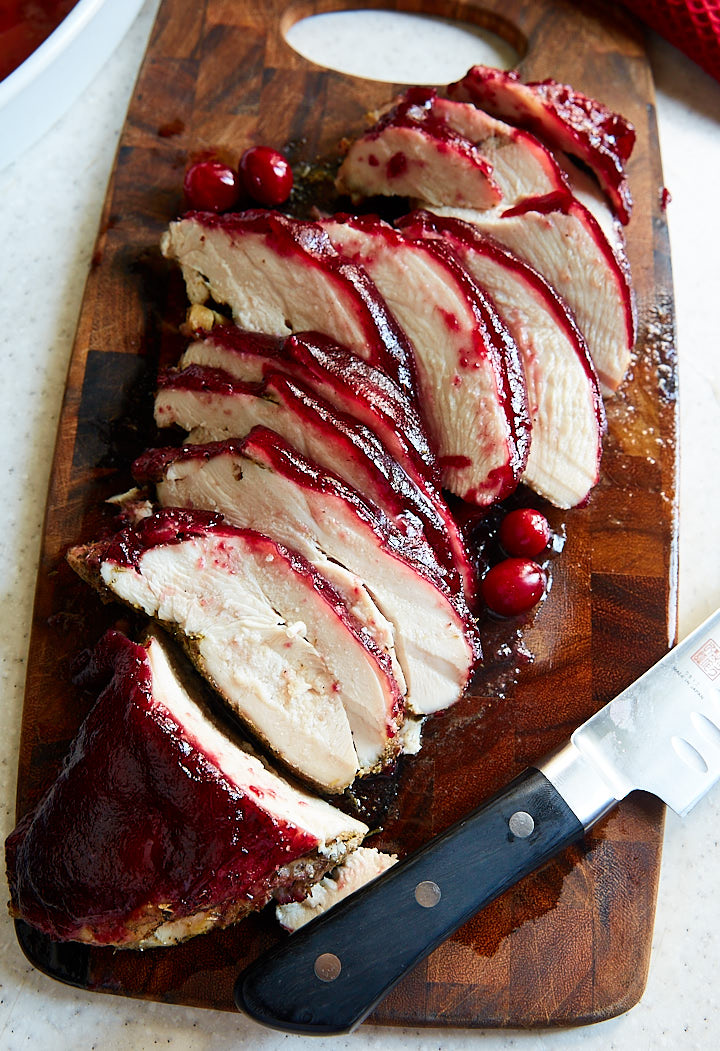 Cranberry glazed turkey breast sliced on a brown cutting board.