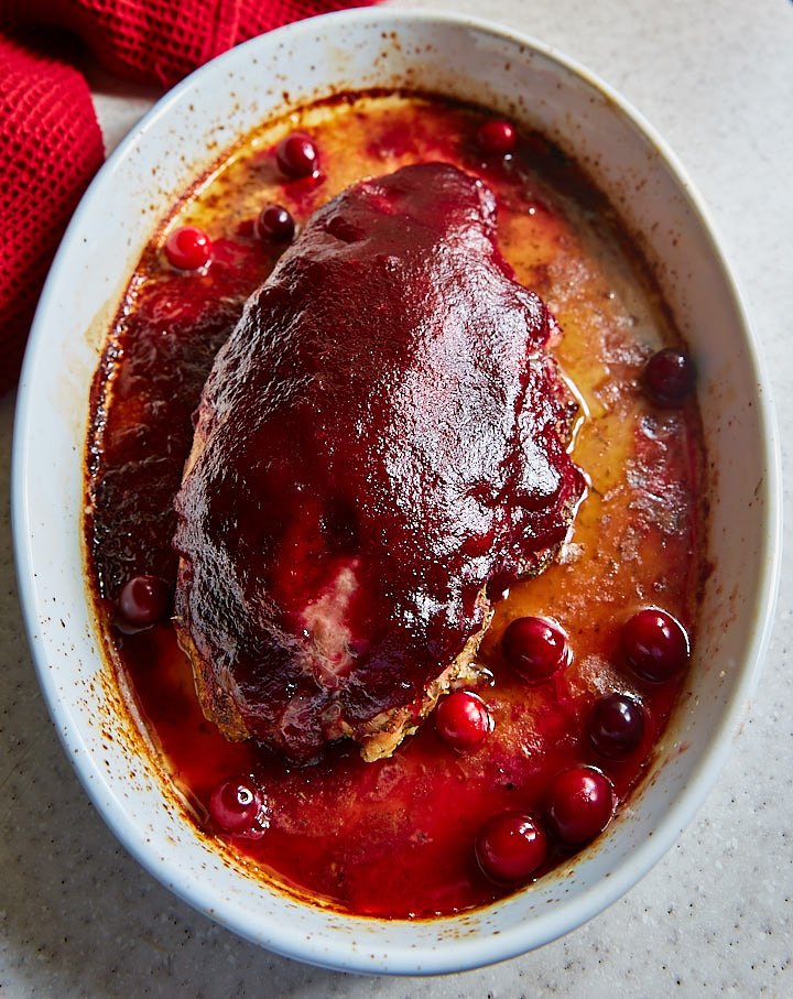 Cranberry glazed turkey breast in a white baking dish, juices on the bottom.