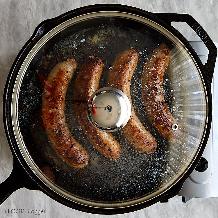 Brats cooking in a pan closed with a lid.