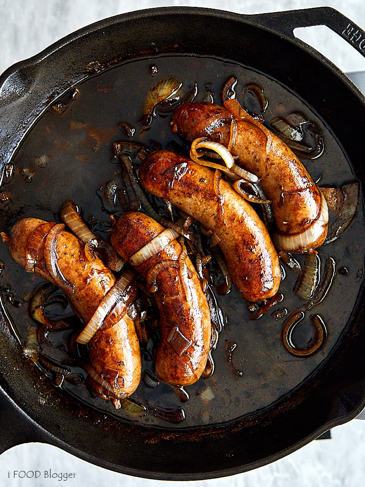 Top down view of brats with beer and onions, fully cooked.