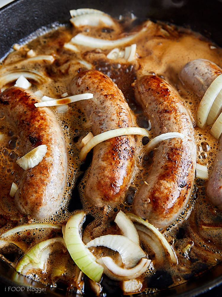 Brats cooking in beer with onions on the stove.
