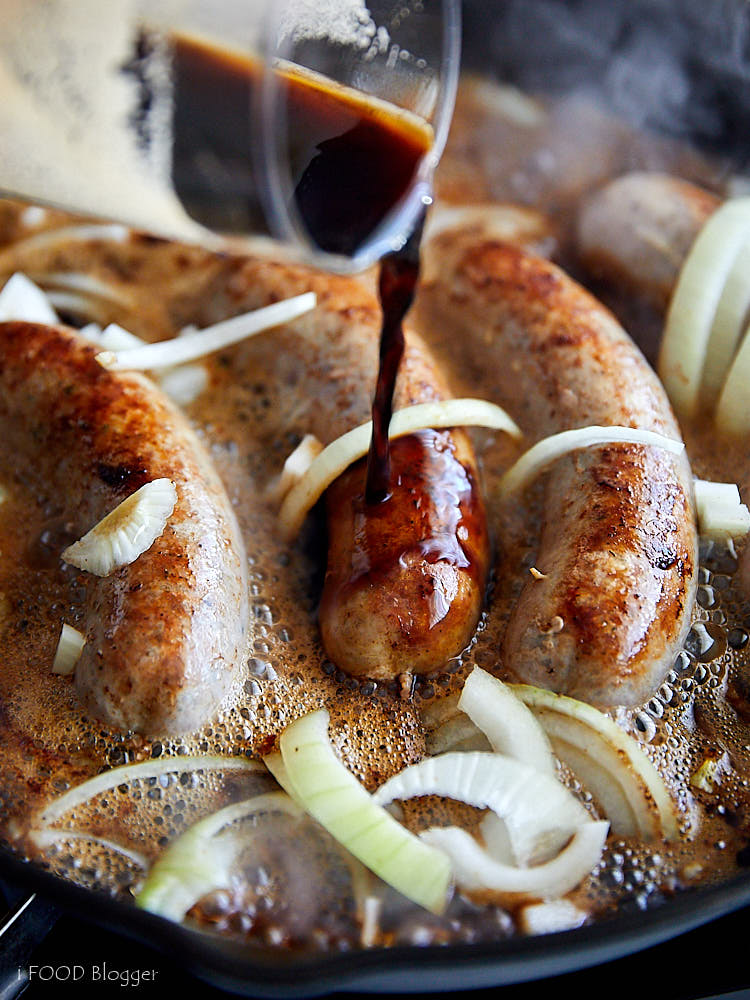 Pouring beer over brats and onions in a cast iron pan.