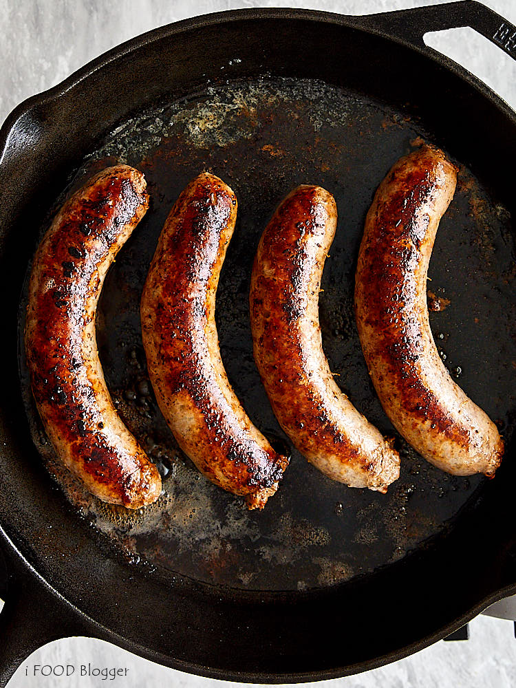 Pan-fried brats, browned and juicy, on a black cast iron pan.