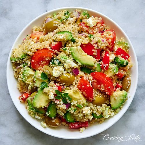 Close up of a Mediterranean salad with tomatoes, avocado, cucumbers, olives and Feta on a white plate.