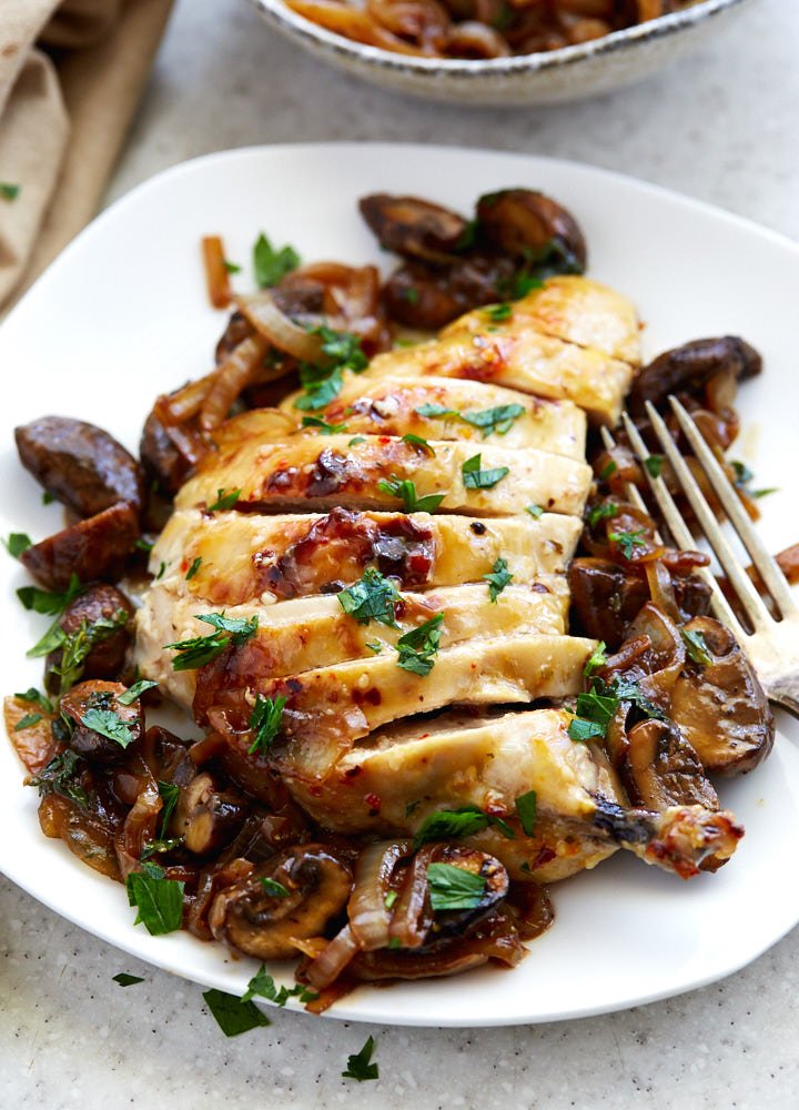 Italian dressing chicken breast sliced on a plate with mushrooms on the side.
