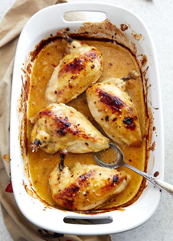 Top down view of four chicken breasts cooked in Italian dressing in a large white baking pan.