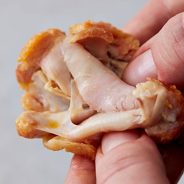 Splitting open baked chicken wing, juices dripping off.