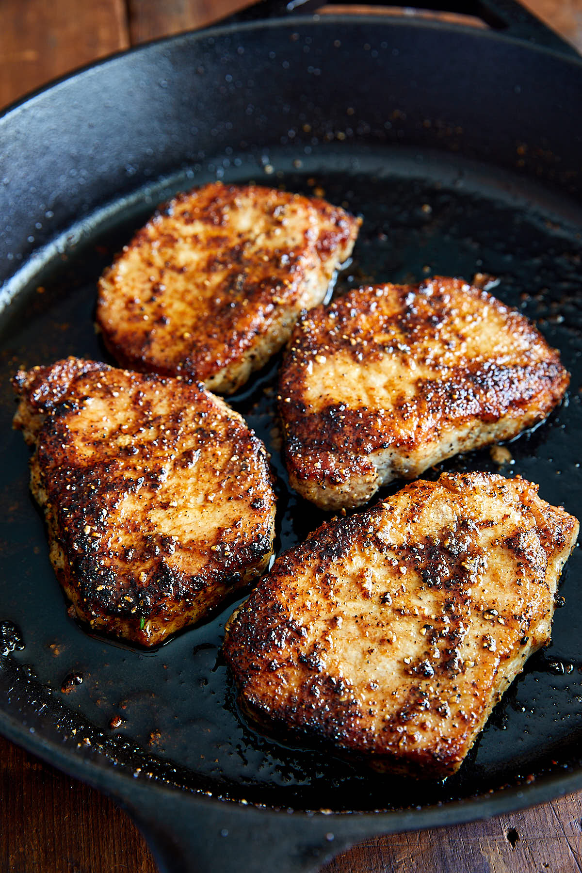 Golden-brown, succulent fried pork chops in a cast iron pan.