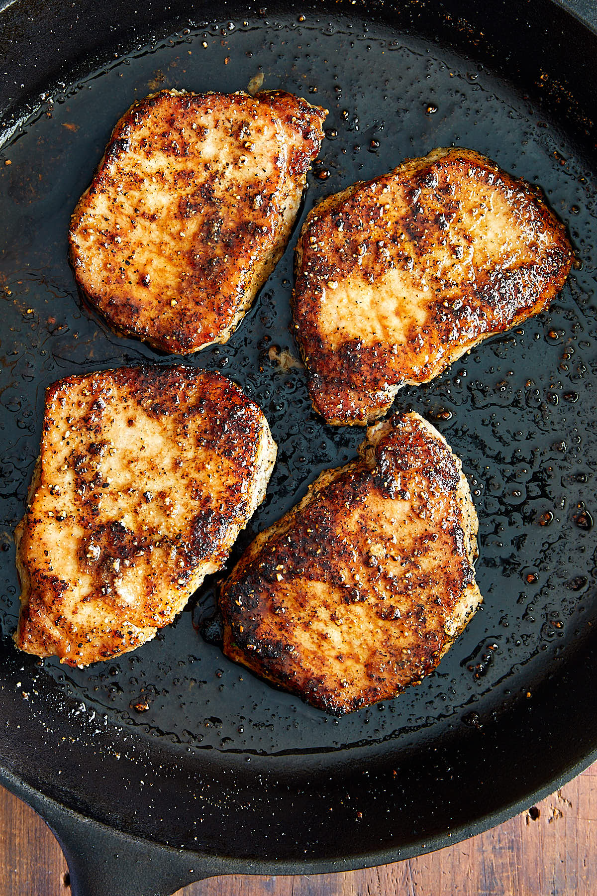 Top down close up view of four well-browned, juicy pork chops inside a cast iron pan.