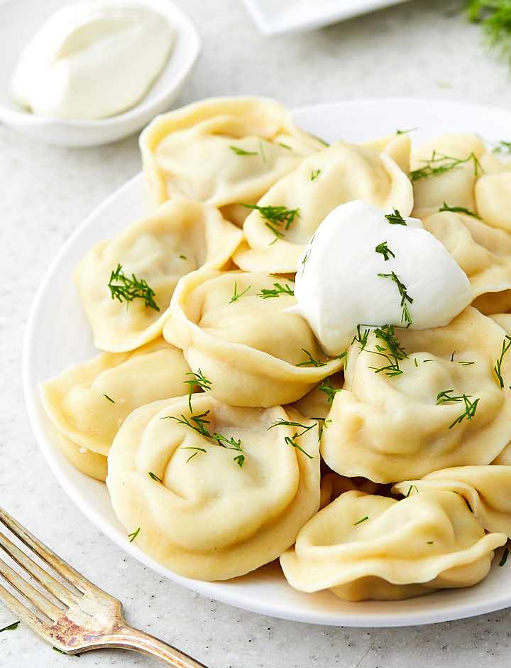 A bowl of Russian pelmeni with a dollop of sour cream on top and sprinkled with chopped dill weed.