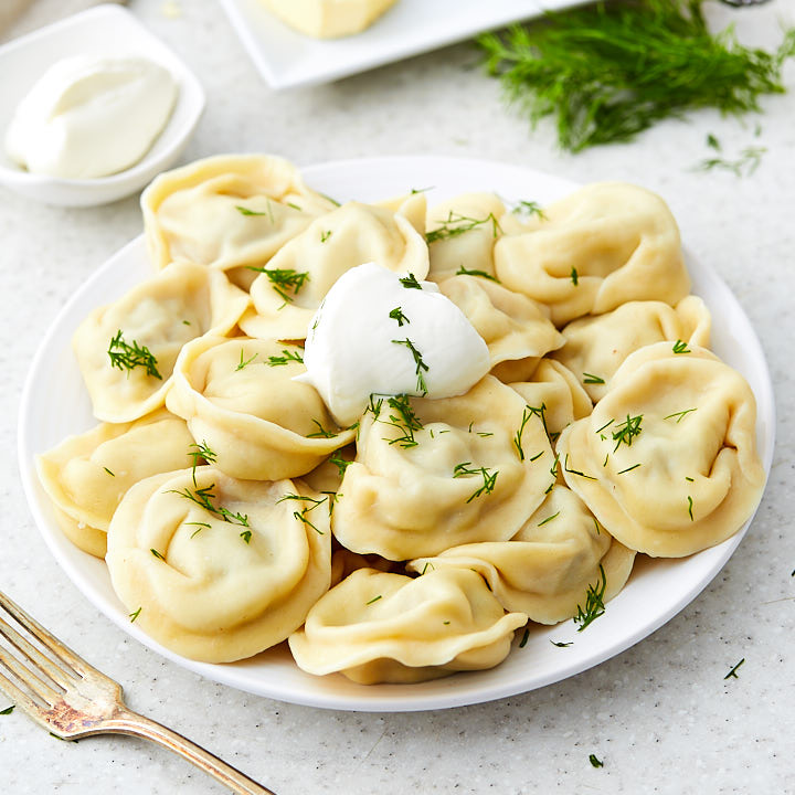 A white bowl of pelmeni with sour cream and chopped dill on top.