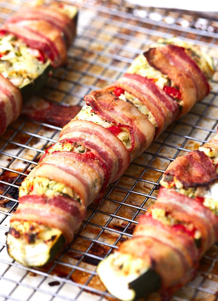 Close up of a bacon-wrapped stuffed zucchini boat on a baking sheet.