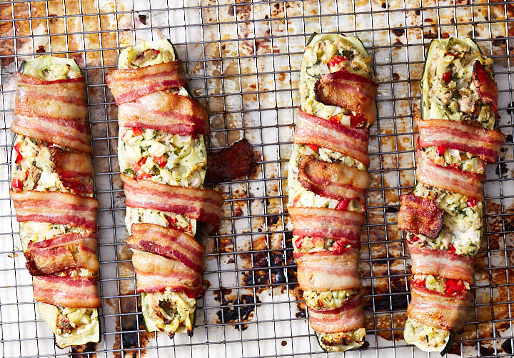 Chopped vegetables and cream cheese stuffed zucchini boats on a baking sheet.