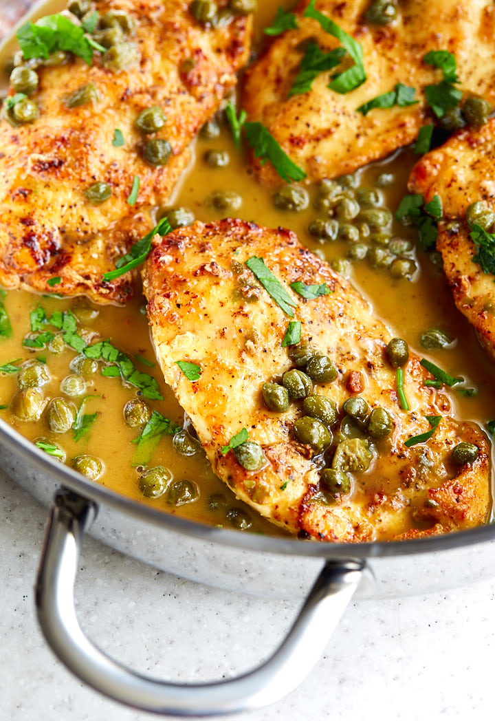 Close up of golden-brown chicken piccata pieces in a saute pan with juices on the bottom of the pan.