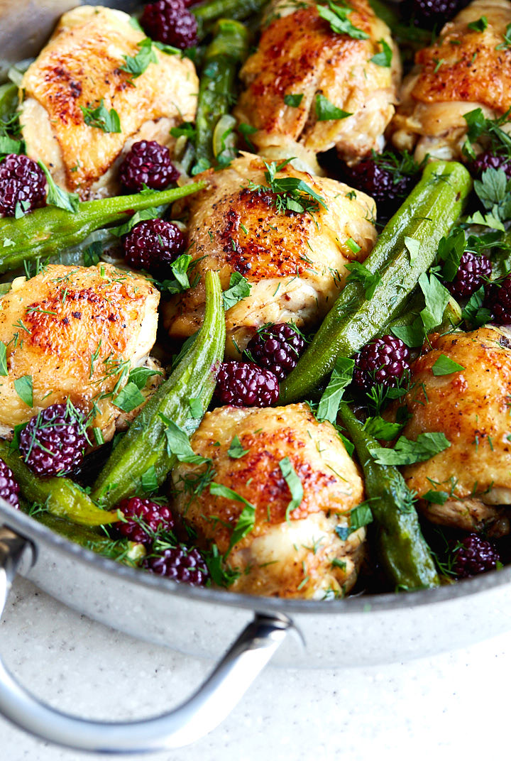 Chicken thighs with okra and blueberries in a pan.