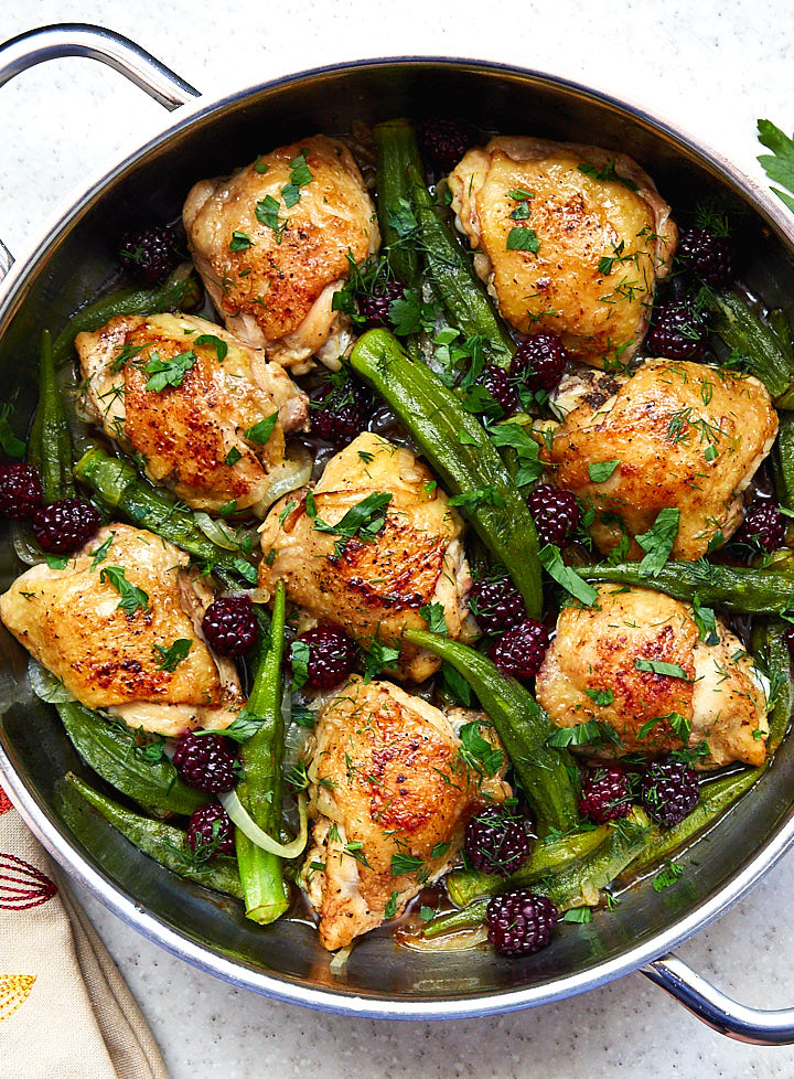 Chicken with okra and blueberries garnished with chopped parsley in a saute pan.