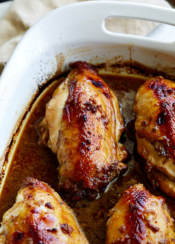 Asian chicken, with golden brown tops, in a white baking dish with dark brown juices on the bottom.