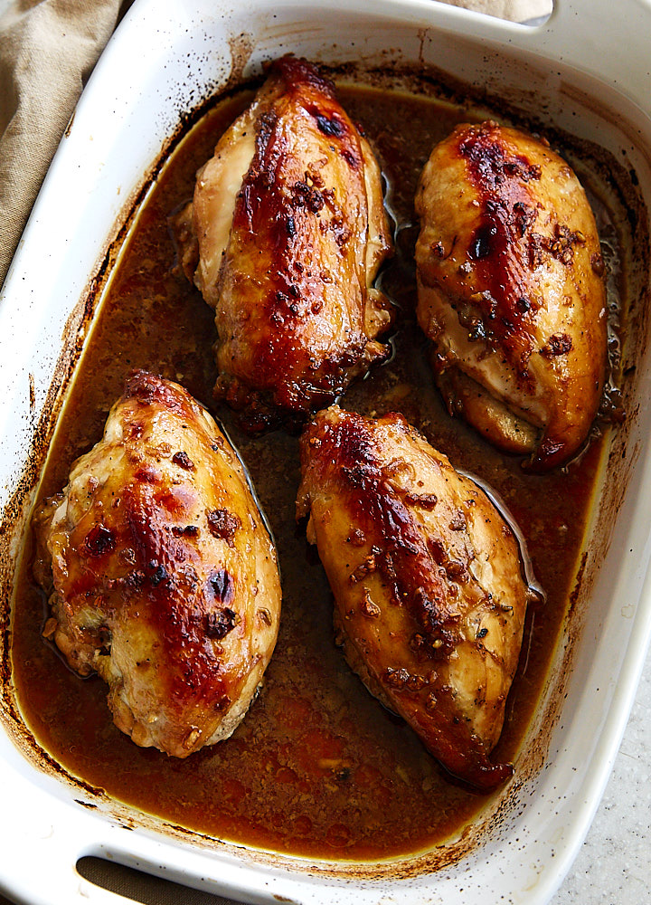 Top down view of Asian chicken breast inside a white baking dish with dark red pan juices on the bottom.