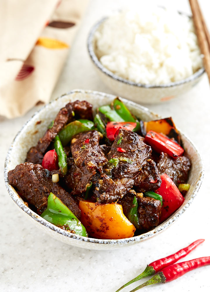 Hunan beef with peppers and asparagus in a bowl, next to a bowl with white rice