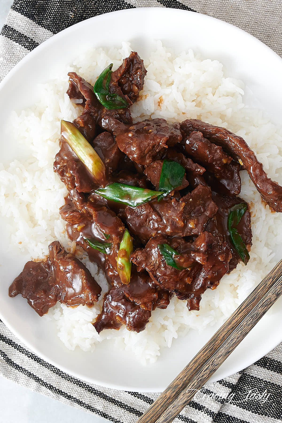 Top down view of a sticky Mongolian beef in a white bowl over white rice.