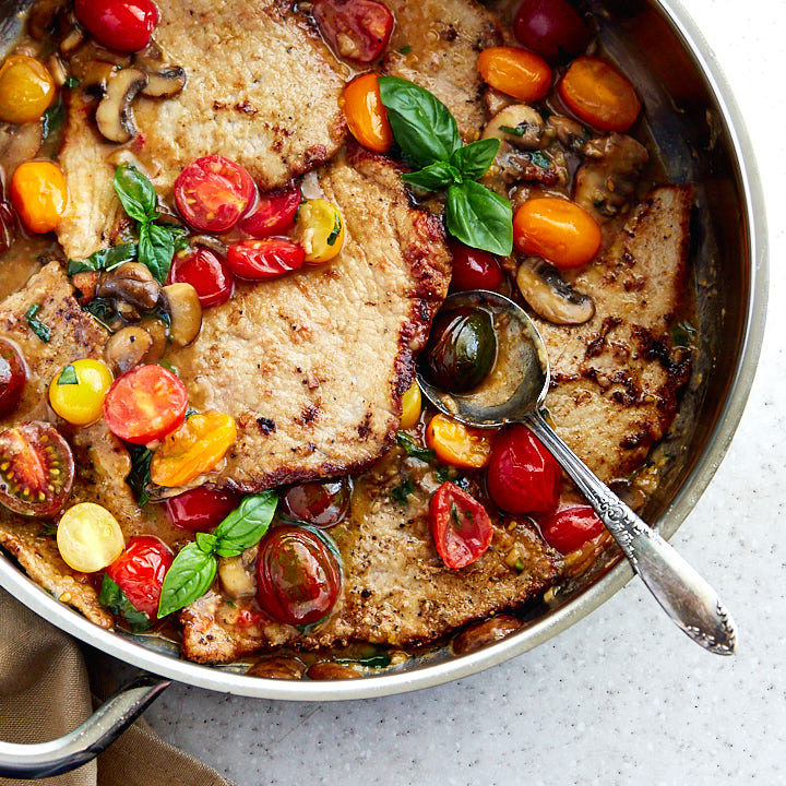 Veal scallopini in a frying pan with sauce, and tomatoes.