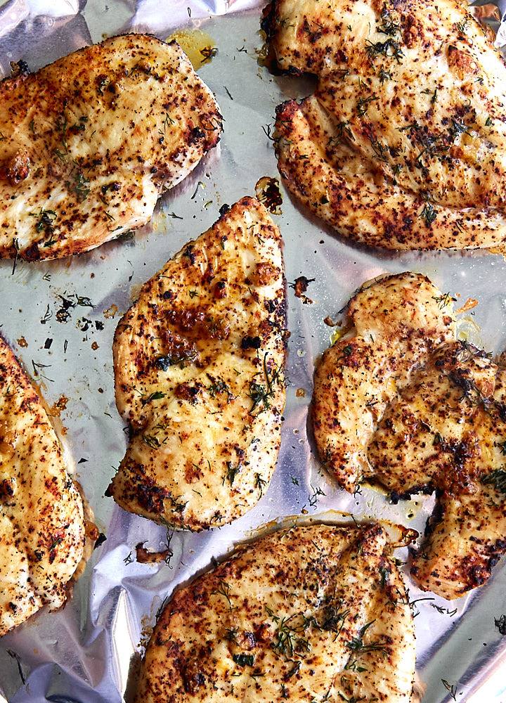 Top down view of golden-brown broiled chicken breast on a baking tray.