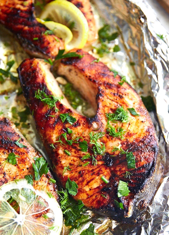 Broiled salmon steak with lemon slices on foil.