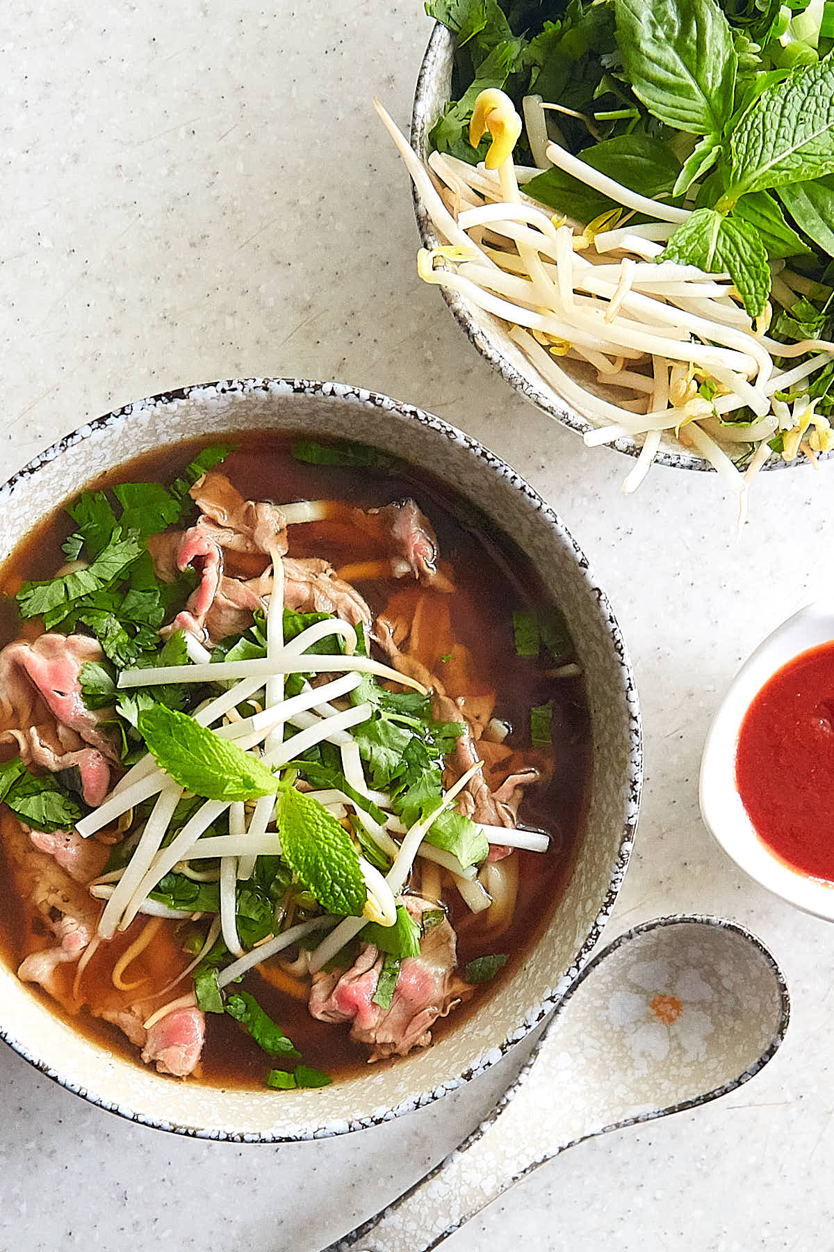 Top down view of Vietnamese pho soup on a bowl garnished with bean sprouts, mint and parsley.