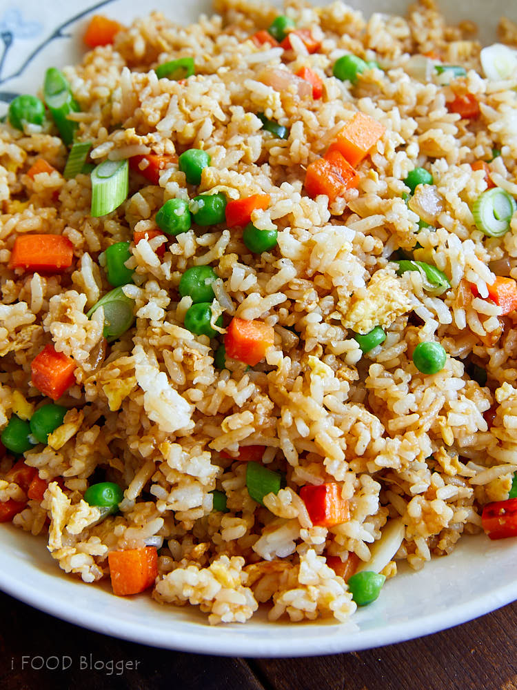 A close up of bowl of hibachi rice with peas, green onions and diced carrots.