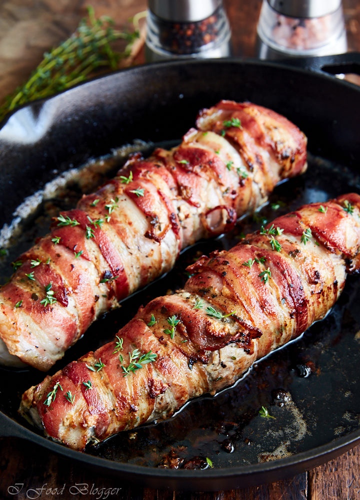 Close up of crispy bacon-wrapped pork tenderloins sprinkled with chopped greens.