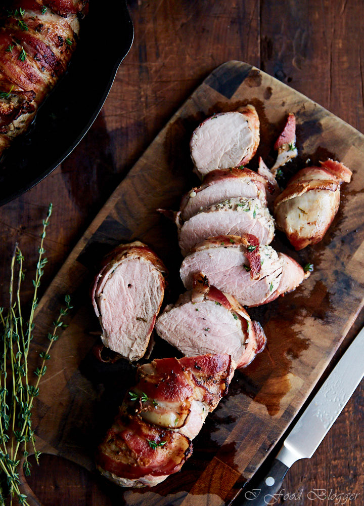 bacon-wrapped pork tenderloins sliced into pieces on a wooden cutting board, showing pink, juicy meat inside.