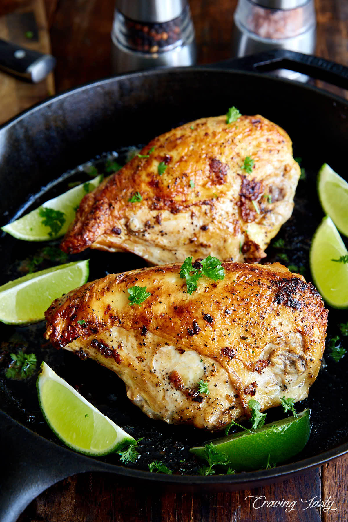 Golden-brown chicken breasts with lime wedges in a cast iron pan.