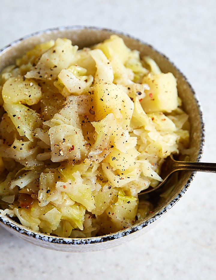 A bowl full with smothered cabbage with a spoon inserted.