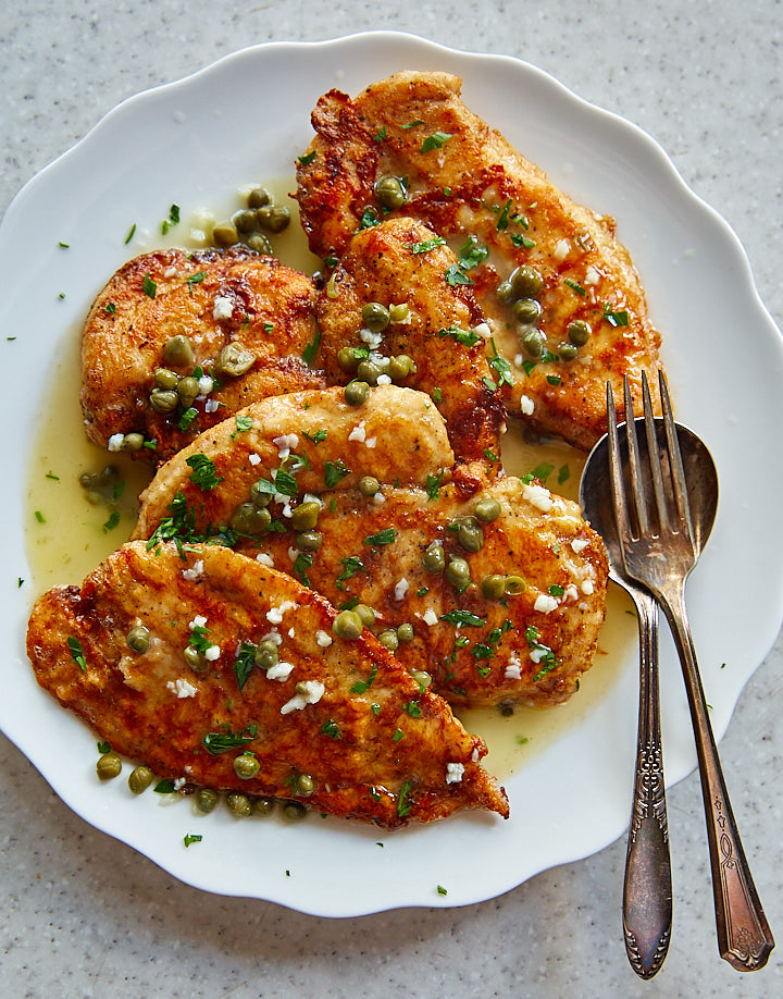 Chicken francese on a white platter, covered with sauce and capers.