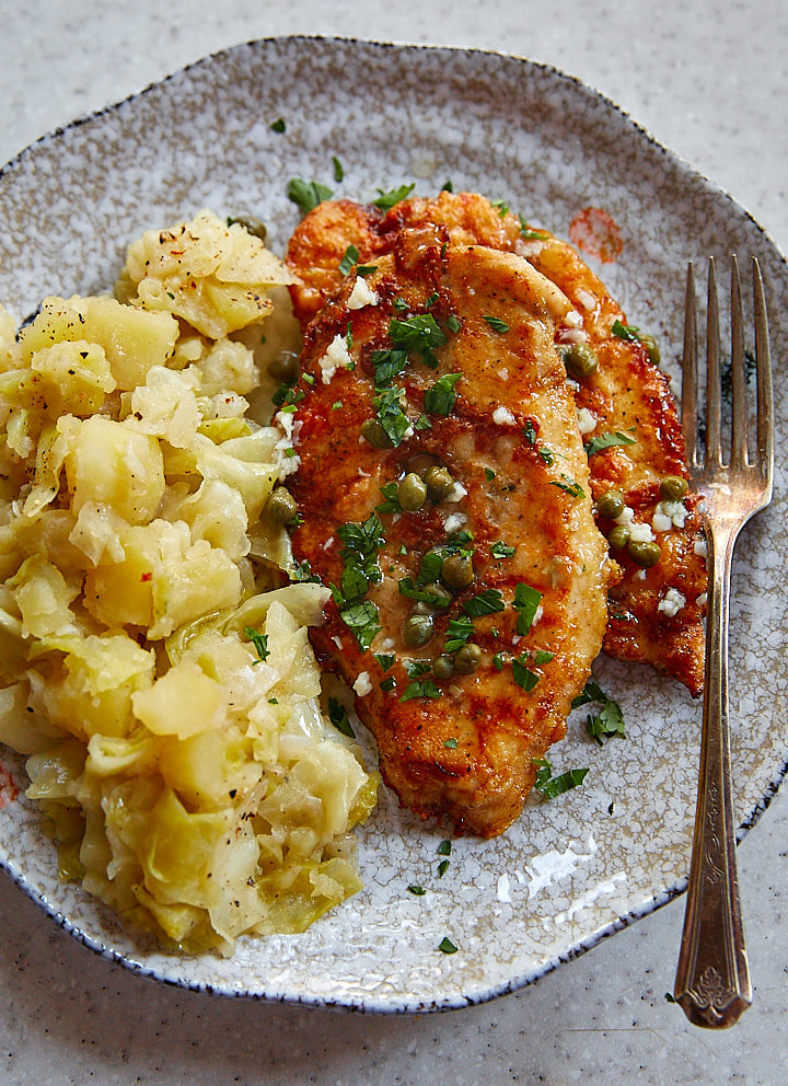 Chicken francese with smothered cabbage on a plate with a fork.