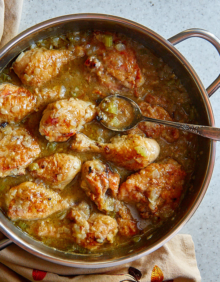 Smothered chicken in a large pan with a spoon inside.