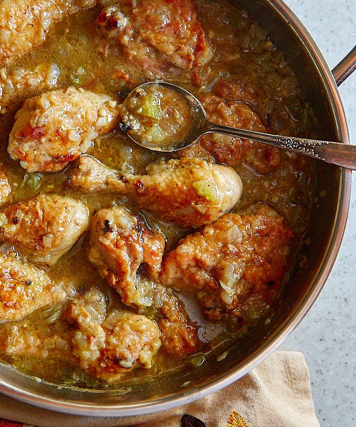 Close up of smothered chicken pieces in a saute pan.