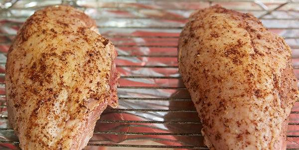 Chicken breasts with dry rub on, on a cooling rack.