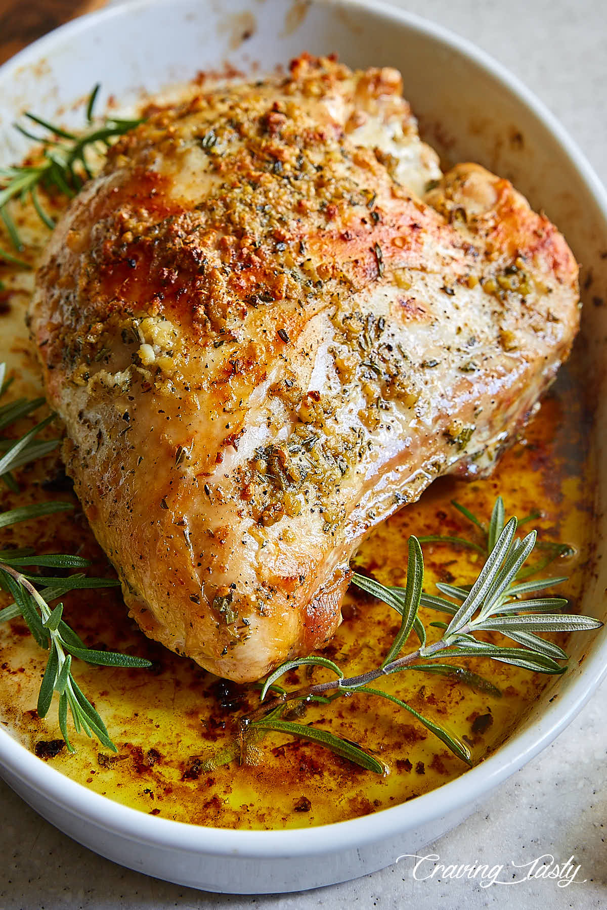 Well-browned turkey breast in a white baking dish garnished with fresh rosemary.