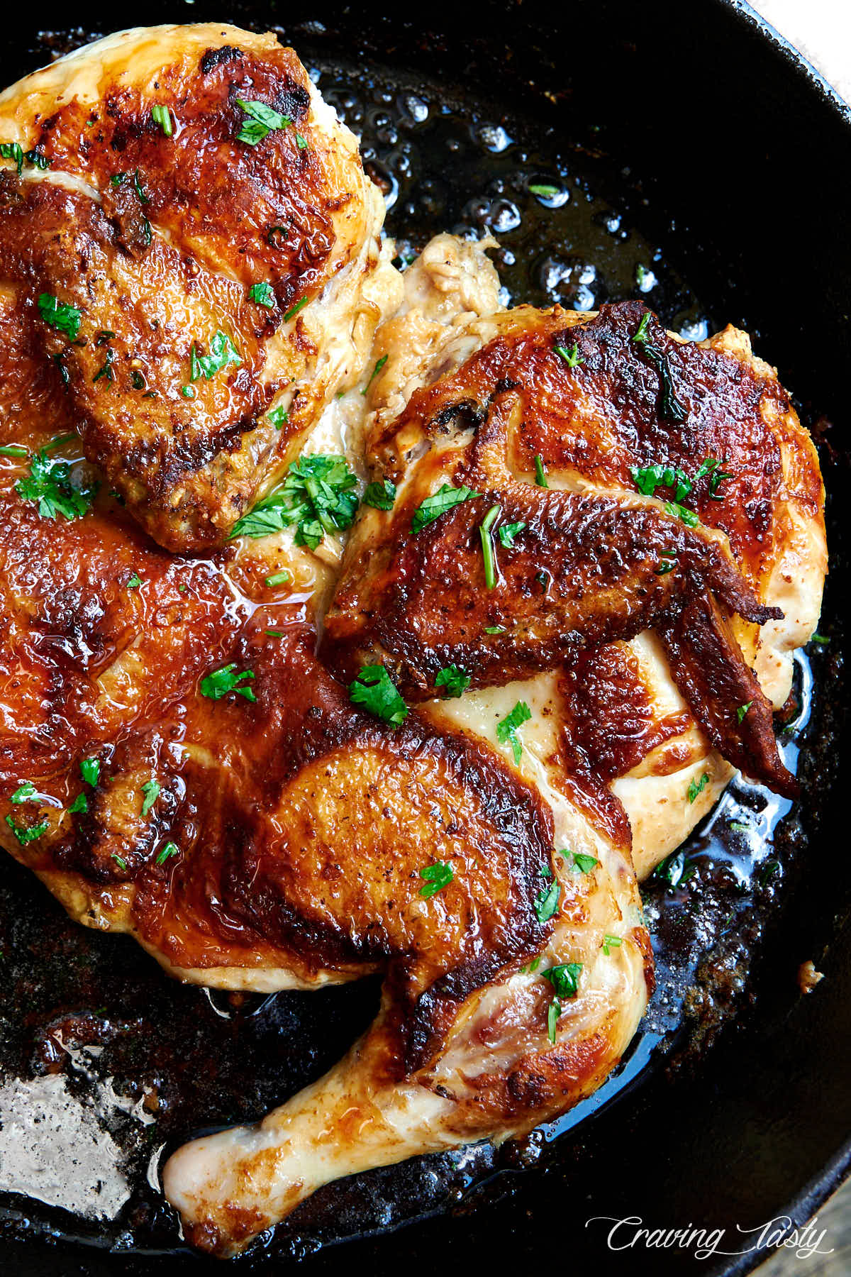 Chicken tabaka with golden-brown skin on a black cast iron pan.