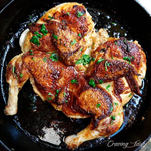 Chicken tabaka with golden-brown skin on a black cast iron pan.